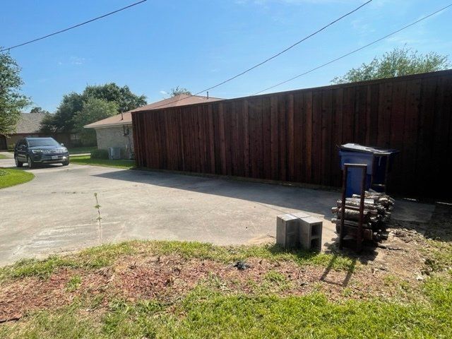 A car is parked in a driveway next to a wooden fence.