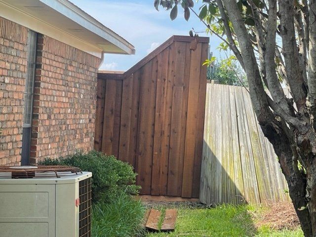 A brick house with a wooden fence and an air conditioner in the backyard.