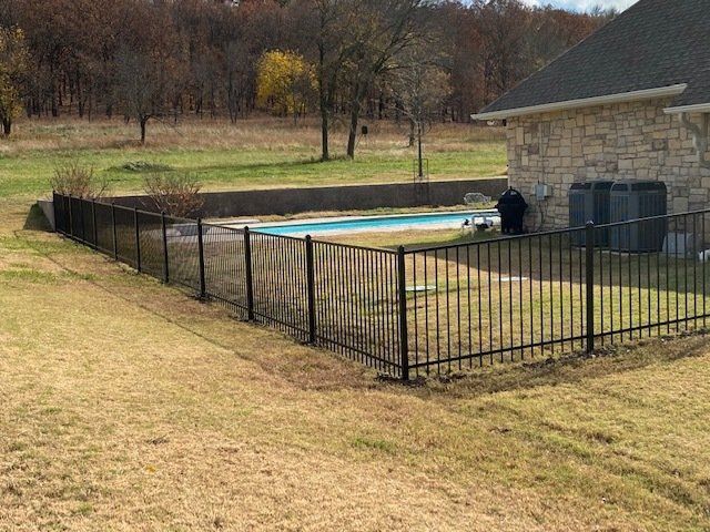 A black fence surrounds a swimming pool in a backyard.
