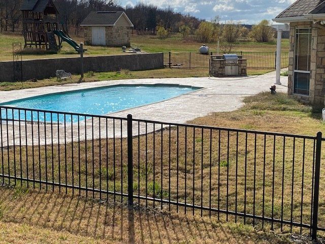 A fence surrounds a large swimming pool in a backyard.