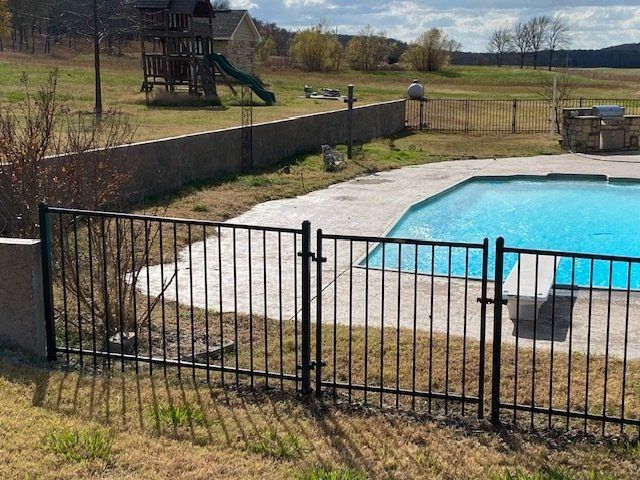 A fence surrounds a swimming pool with a playground in the background