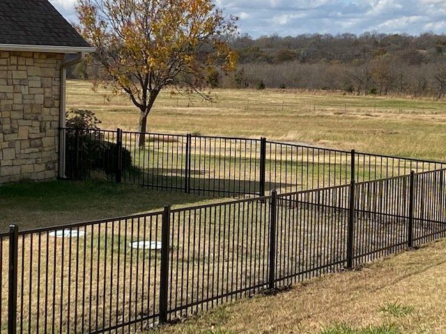 A black metal fence surrounds a grassy field in front of a house.