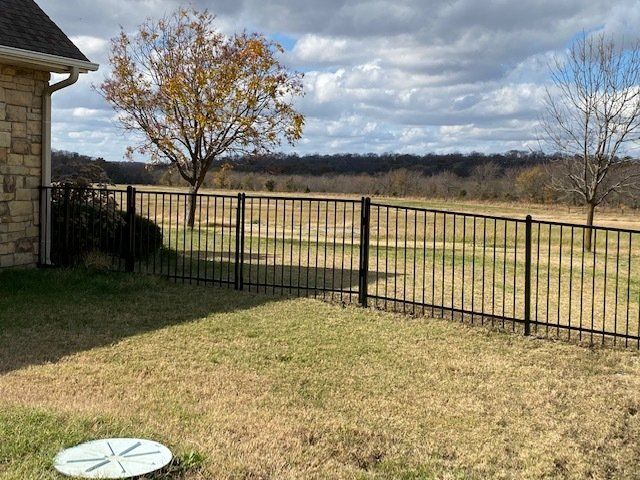 There is a fence in the backyard of a house with a view of a field.