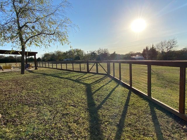 A wooden fence surrounds a grassy field with the sun shining through it.