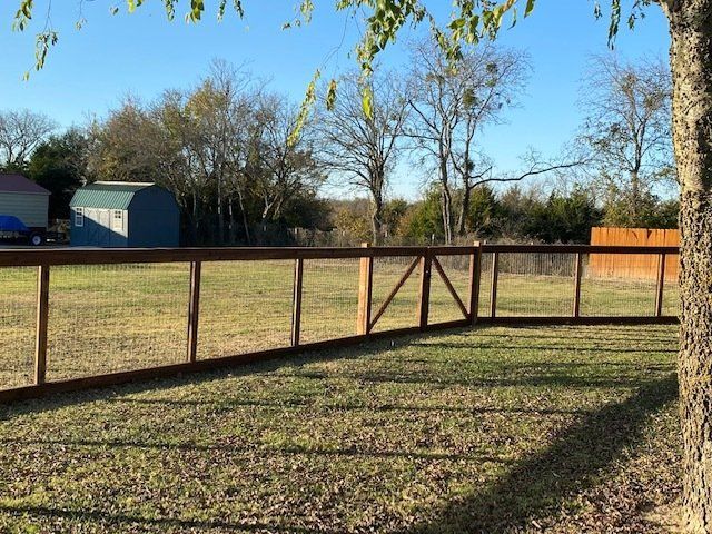 A wooden fence surrounds a grassy field with a tree in the foreground.