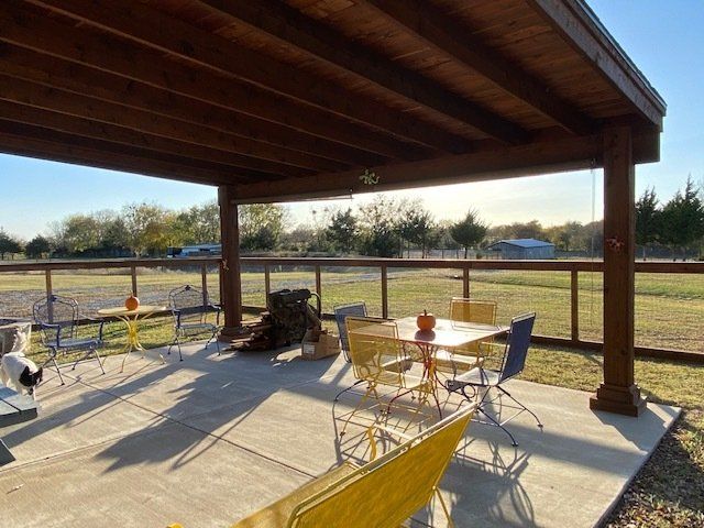 A patio with a table and chairs under a wooden roof.