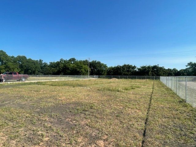 A fence surrounds a grassy field with trees in the background.