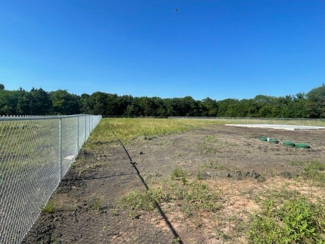 A chain link fence surrounds a field with trees in the background.