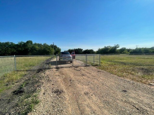 A car is parked on the side of a dirt road next to a fence.
