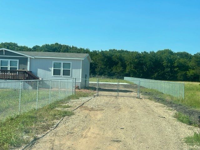 A mobile home is behind a chain link fence on a dirt road.