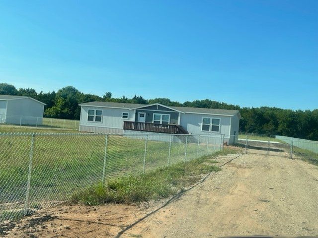 A mobile home is behind a chain link fence in a field.