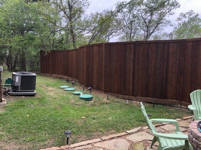 There is a wooden fence in the backyard with a green chair in front of it.