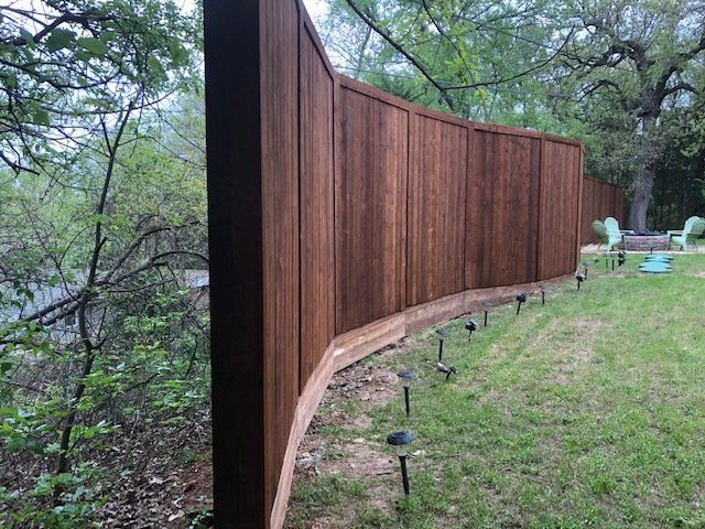 A wooden fence is in the middle of a lush green yard.