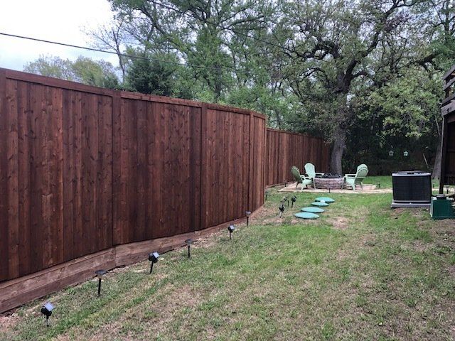 A wooden fence surrounds a lush green lawn in a backyard.