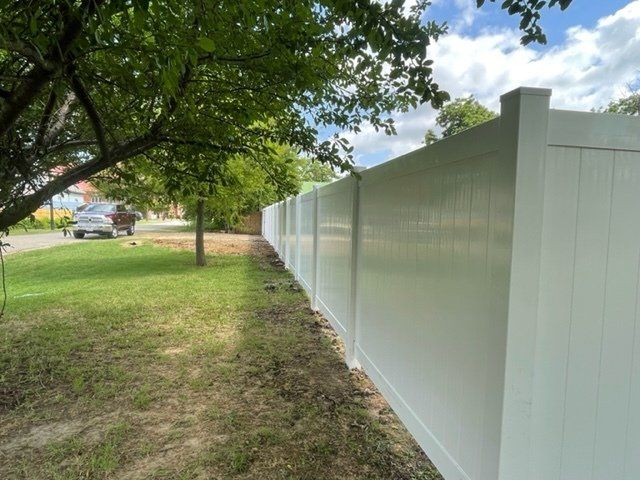 A white fence is surrounded by trees and grass in a yard.
