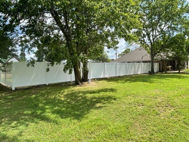 A white vinyl fence is in the backyard of a house.