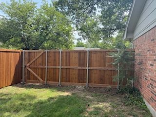 A wooden fence is in the backyard of a brick house.
