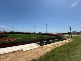 A baseball field with a fence and a blue sky in the background.