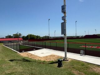 A baseball field with a fence and a fire hydrant in front of it.
