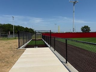A walkway leading to a baseball field with a chain link fence.