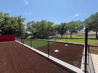 A baseball field with a fence and trees in the background