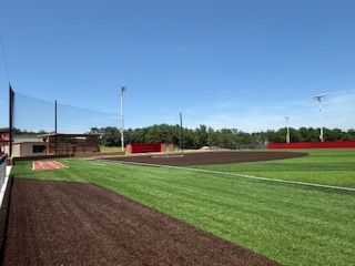 A baseball field with a red fence and a blue sky in the background.