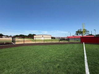 A baseball field with a fence and a few buildings in the background.