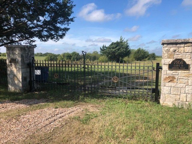 A wrought iron gate is surrounded by a stone wall and grass.