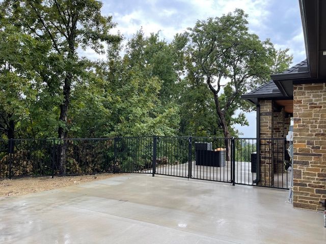 A concrete patio with a metal fence and a brick building in the background.