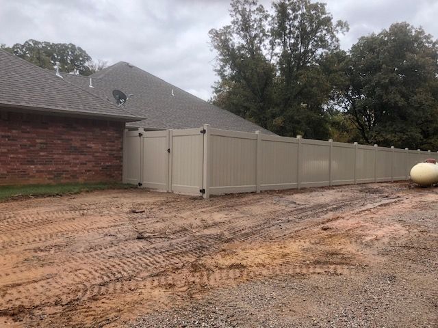 A white fence is surrounding a dirt driveway in front of a house.