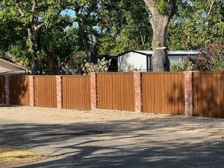A wooden fence is surrounded by bricks and trees in a driveway.
