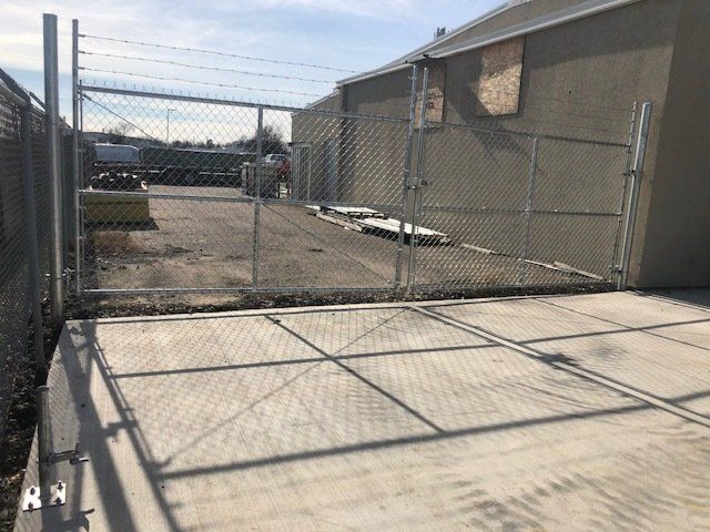A chain link fence surrounds a concrete area in front of a building.