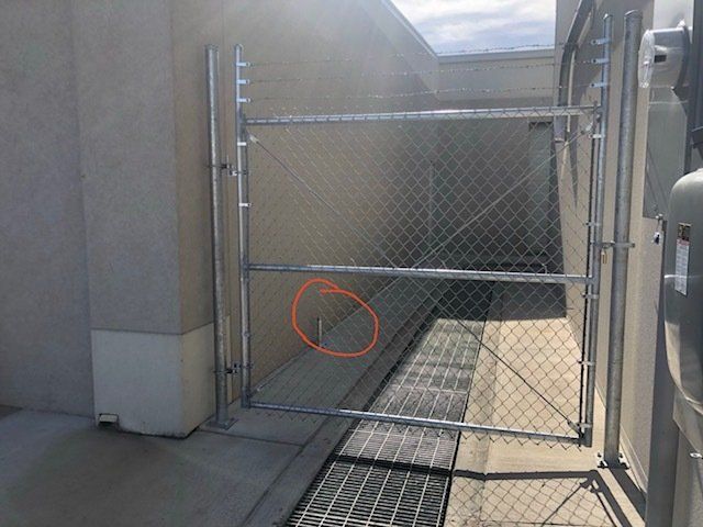 A chain link fence is surrounding a drain on the side of a building.