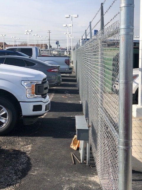 A row of cars are parked behind a chain link fence.