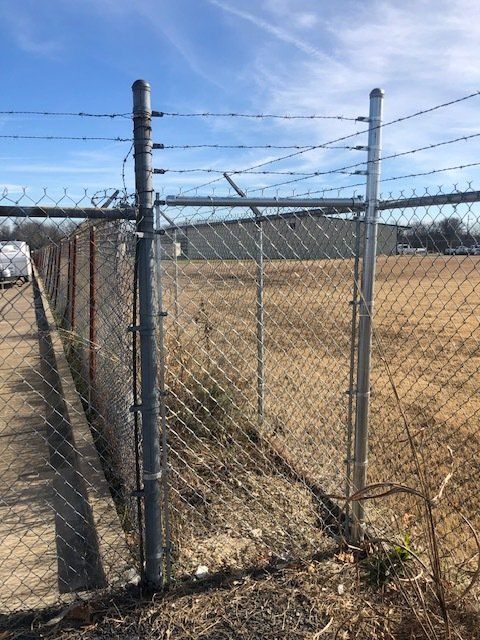 A chain link fence with barbed wire surrounding a field.
