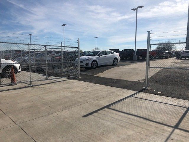 A lot of cars are parked in a parking lot behind a chain link fence.