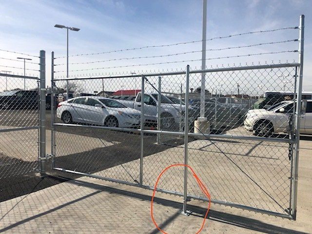 A chain link fence with cars parked behind it.