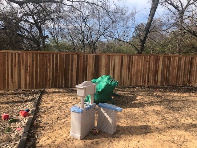 A wooden fence surrounds a sandbox in a backyard.