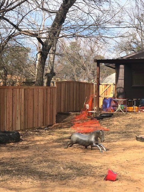A horse statue is sitting in the dirt in front of a wooden fence.