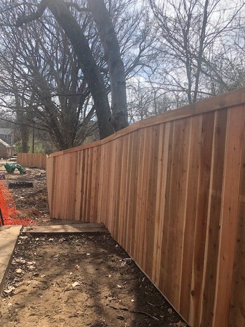 A wooden fence is being built in a yard with trees in the background.