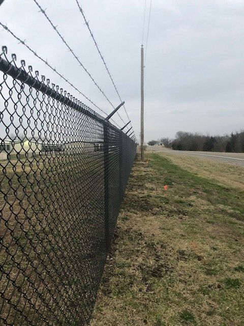 A chain link fence with barbed wire along the side of a road.