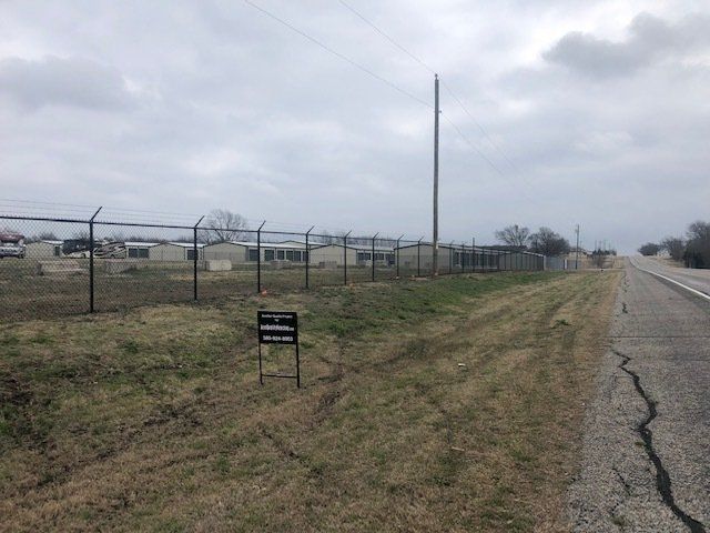 A fence surrounds a grassy field next to a road.