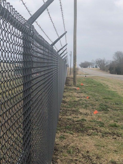A chain link fence with barbed wire along the side of a road.
