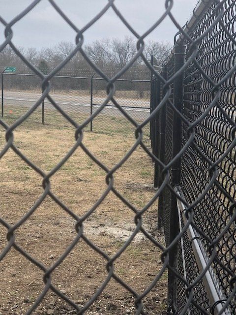 A chain link fence surrounds a field with a road in the background.