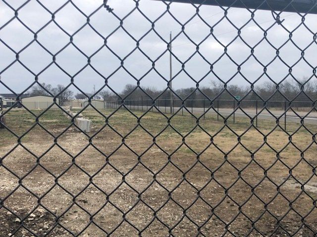 A chain link fence looks out over a dirt field
