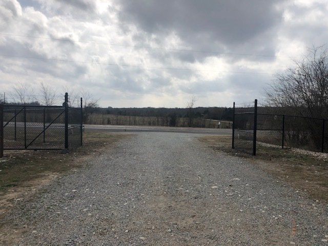 A gravel road with a fence and a cloudy sky in the background.