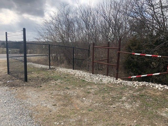 A chain link fence is surrounded by trees and a gravel road.