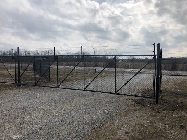 A chain link fence is surrounding a gravel road.
