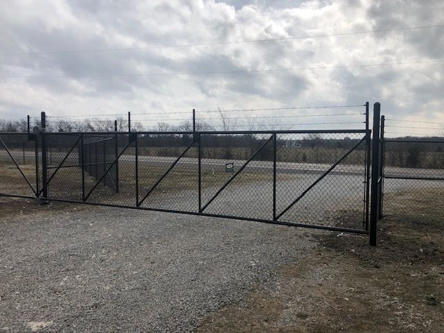 A chain link fence is surrounding a gravel road.