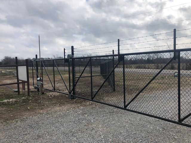 A chain link fence with barbed wire surrounding a gravel road.